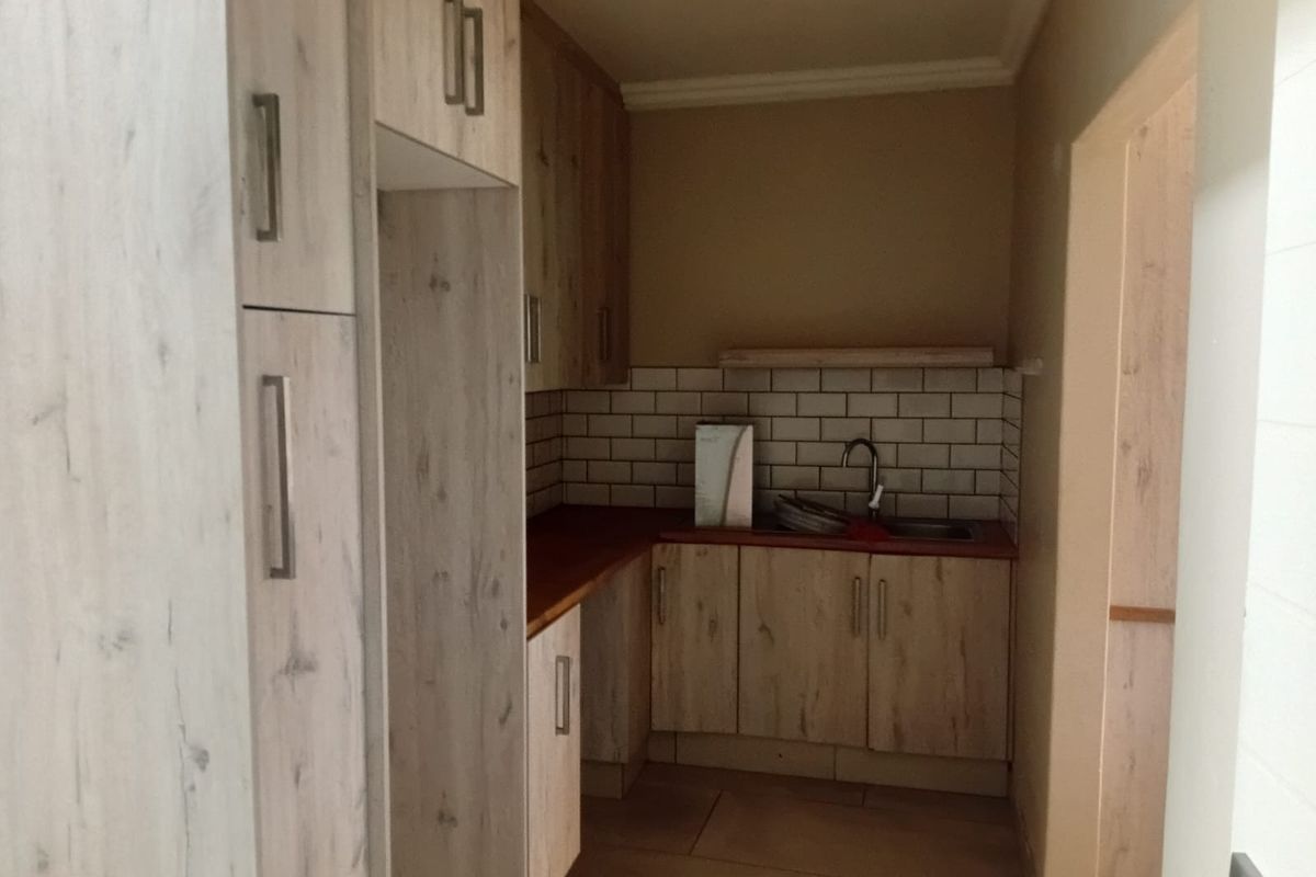 A compact kitchen featuring light wood-look cabinetry, a subway tile backsplash, and a wooden countertop with an integrated sink.