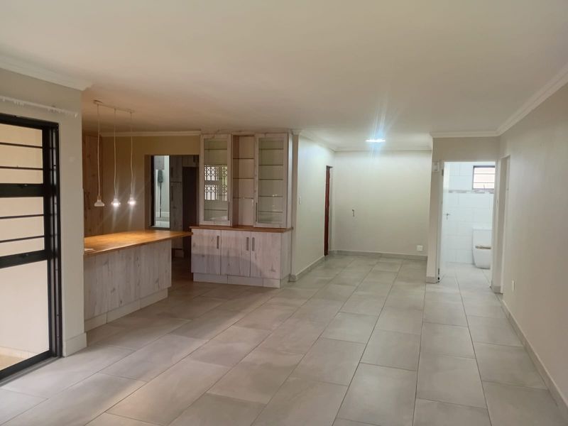 Spacious open-plan living area featuring large format floor tiles, built-in cabinetry with a breakfast bar, and neutral finishes throughout.