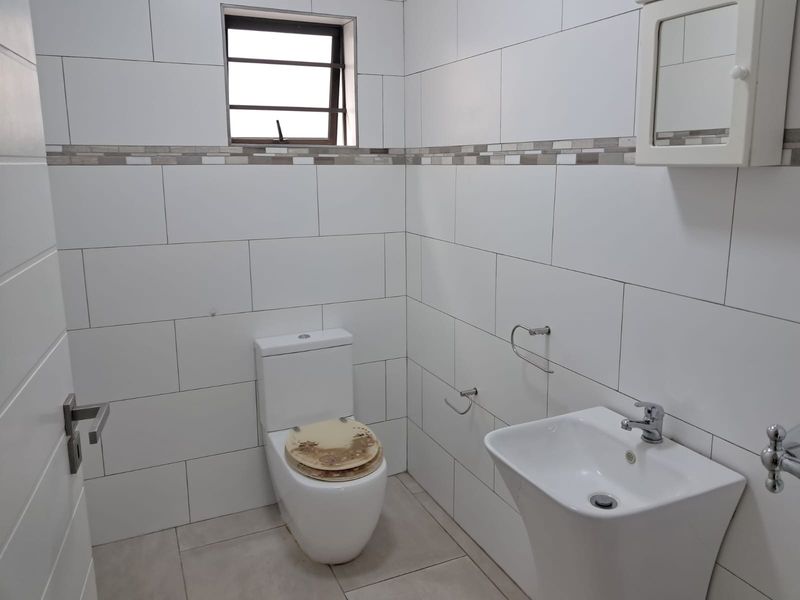 A clean, modern bathroom featuring white wall tiles with a decorative border, a pedestal basin, and a standard toilet.