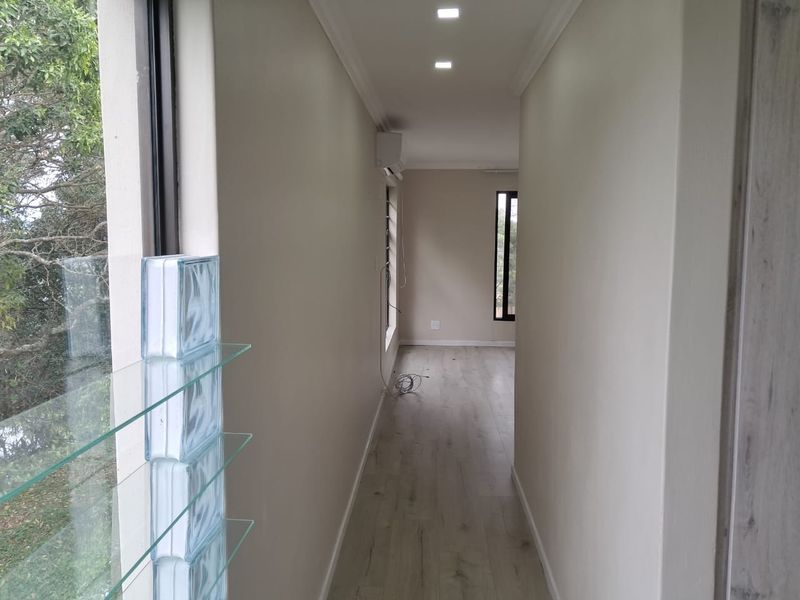 A bright, empty hallway featuring modern laminate flooring, recessed downlighting, and an air conditioning unit, leading towards an open living space.