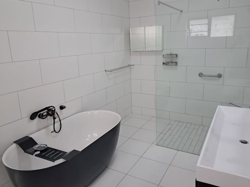 Modern bathroom featuring a sleek freestanding bathtub, a spacious walk-in shower with glass screen, and contemporary white subway tiling.