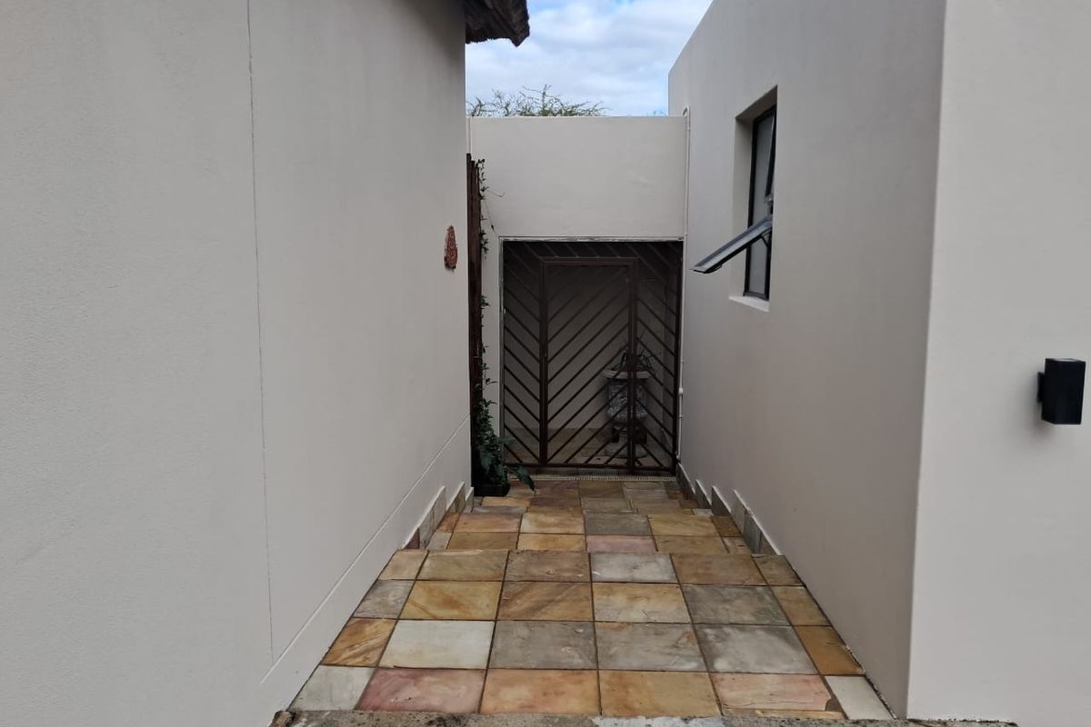 A paved exterior walkway leading to a secure gated entrance, featuring neutral rendered walls and external lighting.