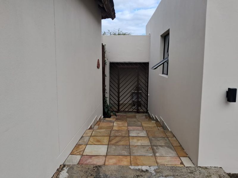 A paved exterior walkway leading to a secure gated entrance, featuring neutral rendered walls and external lighting.