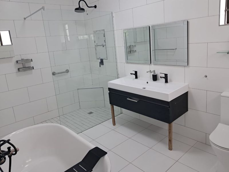 Modern bathroom featuring a freestanding bathtub, a spacious walk-in shower with glass screen, and a contemporary double vanity with wall-mounted mirrors.