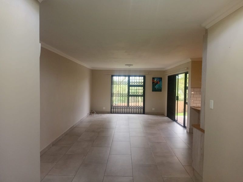 Spacious open-plan living area featuring neutral tiled flooring, coved ceilings, and direct access to the outdoors through a secure sliding glass door.