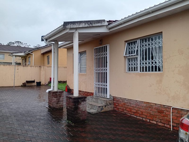 Rear exterior view of the property featuring a paved courtyard, covered patio area, and security features on windows and doors.