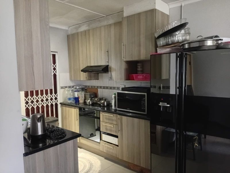 A functional kitchen featuring wood-look cabinetry, granite countertops, a built-in oven, and an extractor fan, with a security gate leading to the exterior.