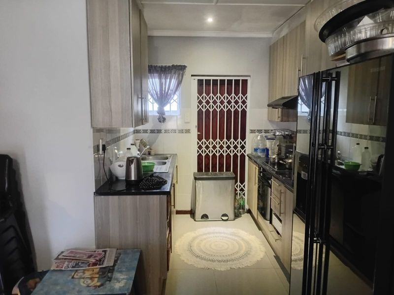 A functional galley-style kitchen featuring light wood-finish cabinetry, dark countertops, built-in oven, extractor fan, and a security gate leading to the exterior.