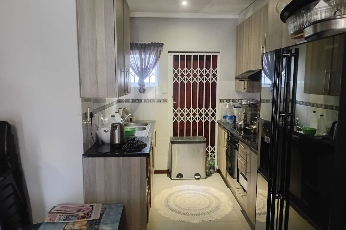 A functional galley-style kitchen featuring light wood-finish cabinetry, dark countertops, built-in oven, extractor fan, and a security gate leading to the exterior.