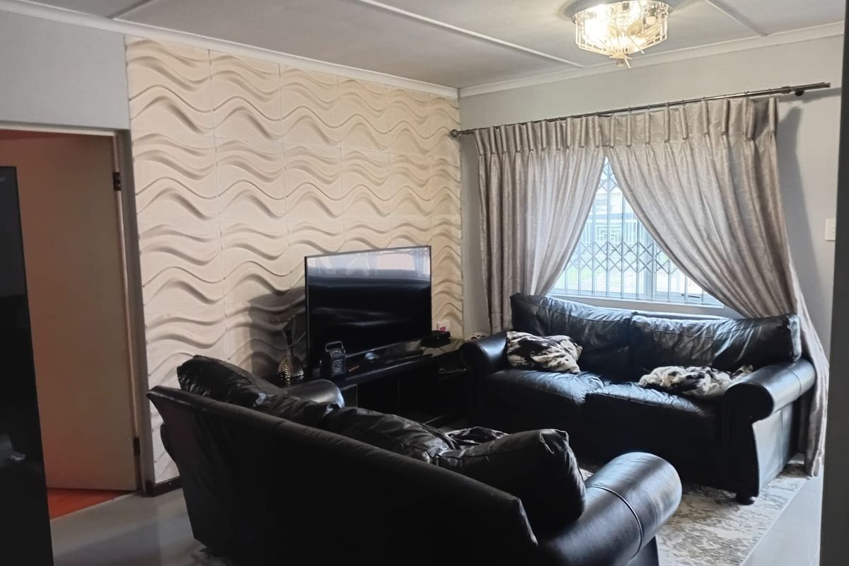 A comfortable living room featuring a textured accent wall, tiled flooring, and a window fitted with a security gate.