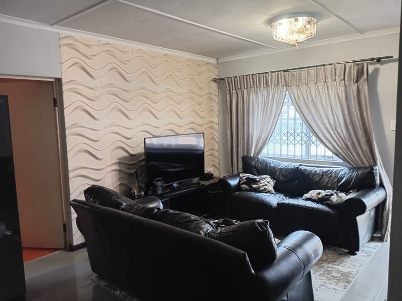 A comfortable living room featuring a textured accent wall, tiled flooring, and a window fitted with a security gate.