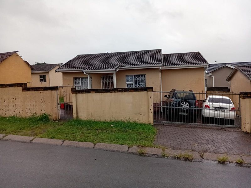 Front view of a single-story house featuring a tiled roof, paved driveway, and perimeter wall with metal security gates.
