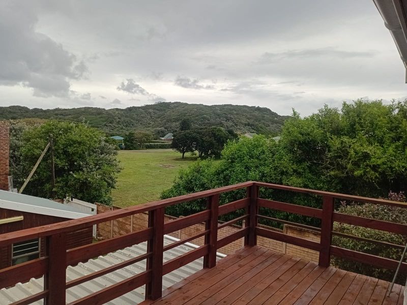 An elevated wooden balcony featuring a timber balustrade, offering scenic views of the surrounding landscape and greenery.