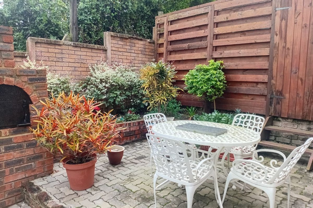 A private rear courtyard featuring a brick-built braai, paved patio area, and enclosed by a combination of brick walls and timber fencing.