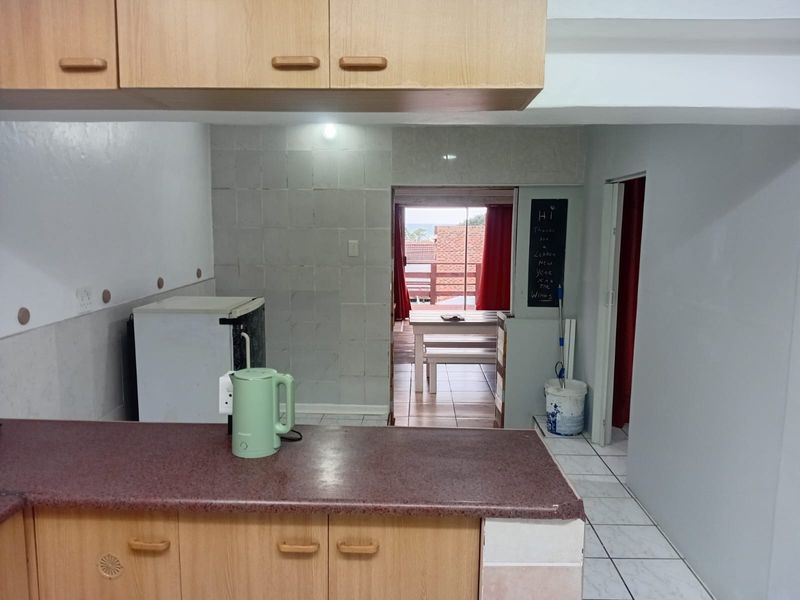 A functional kitchen area featuring laminate cabinetry, tiled splashbacks, and tiled flooring, with a view through to the adjacent patio area.