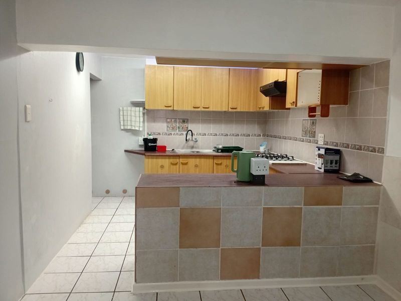 A functional kitchen featuring wooden cabinetry, tiled backsplash, gas hob, and a breakfast bar, requiring some cosmetic updates to improve its overall appeal.