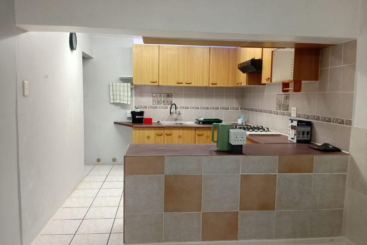 A functional kitchen featuring wooden cabinetry, tiled backsplash, gas hob, and a breakfast bar, requiring some cosmetic updates to improve its overall appeal.