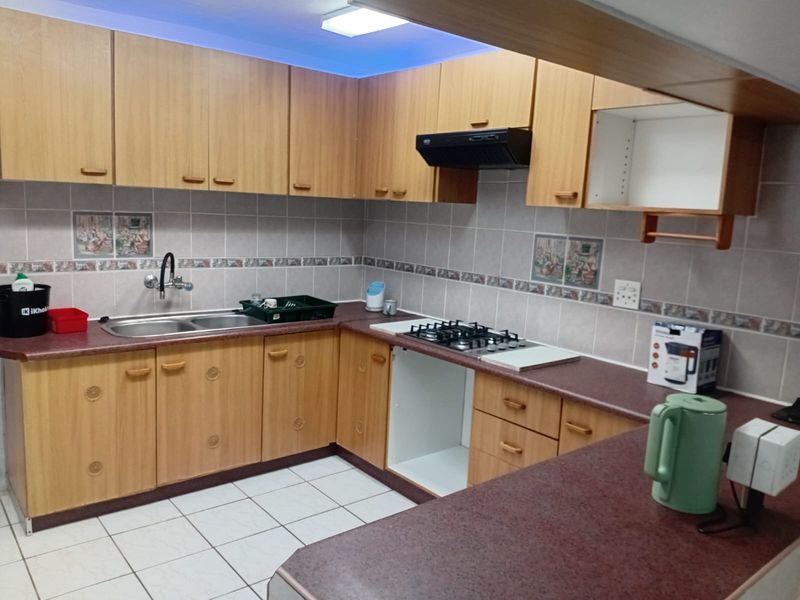 A dated kitchen featuring laminate cabinetry, a gas hob with extractor fan, double bowl sink, and tiled backsplash with a breakfast counter.