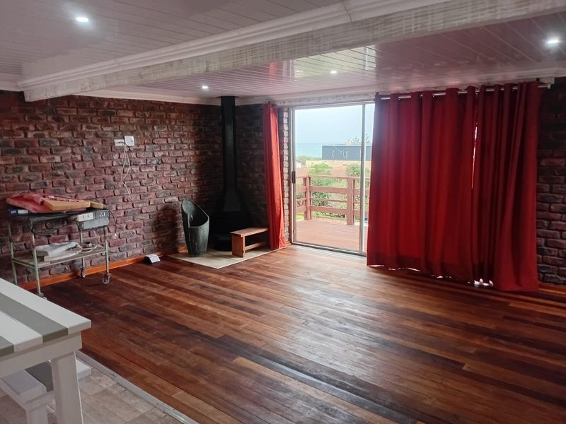 Spacious living area featuring exposed brick walls, rich wood flooring, a built-in fireplace, and direct access to an outdoor balcony with views.