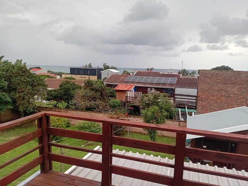 Elevated view from a wooden balcony overlooking a residential neighborhood with a glimpse of the ocean in the distance.