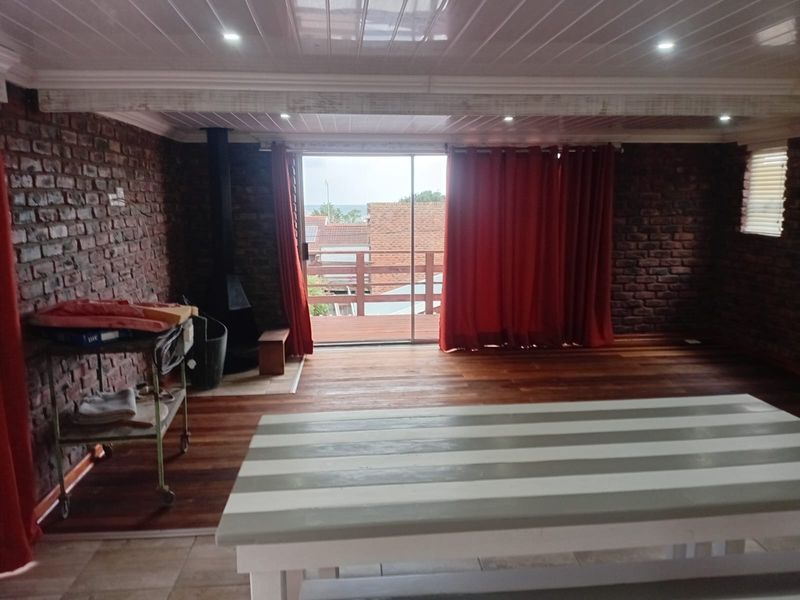 Spacious living area featuring exposed brick walls, hardwood flooring, a freestanding fireplace, and sliding glass doors leading to an outdoor balcony.