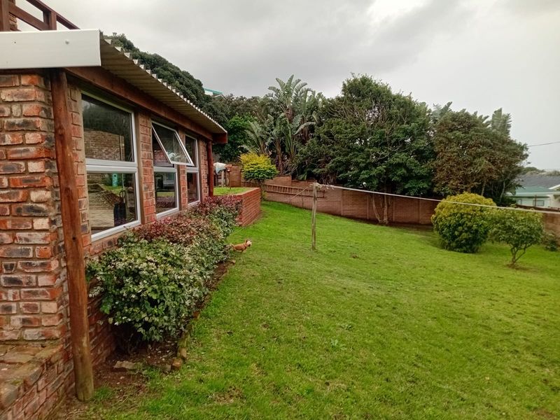 A view of the rear exterior featuring a brick facade, aluminium windows, and a spacious private garden with a brick boundary wall.
