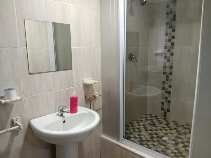 A functional bathroom featuring a pedestal washbasin, wall-mounted mirror, and a tiled shower enclosure with a glass door.
