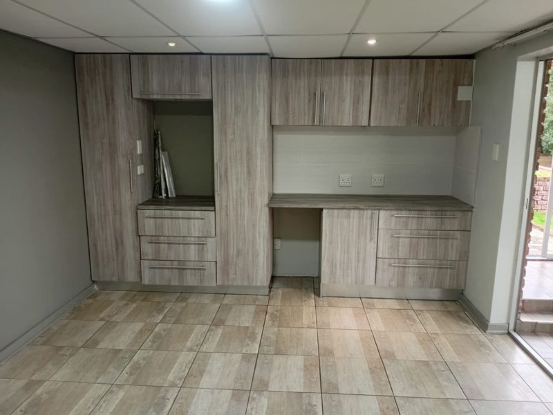 A clean, modern kitchen area featuring light wood-grain cabinetry, ample counter space, tiled flooring, and a drop ceiling with recessed lighting.