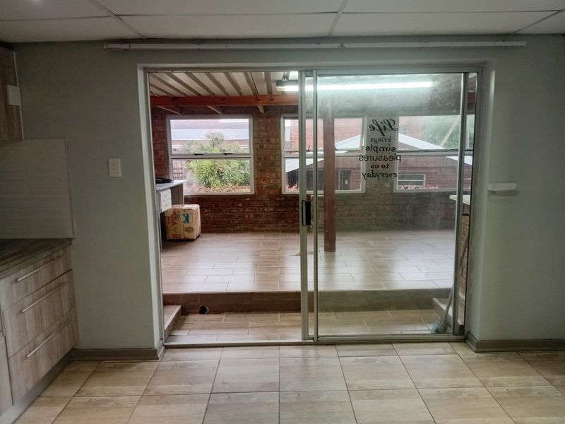 A covered patio area featuring exposed brick walls, timber ceiling beams, and tiled flooring, accessible through a sliding glass door.