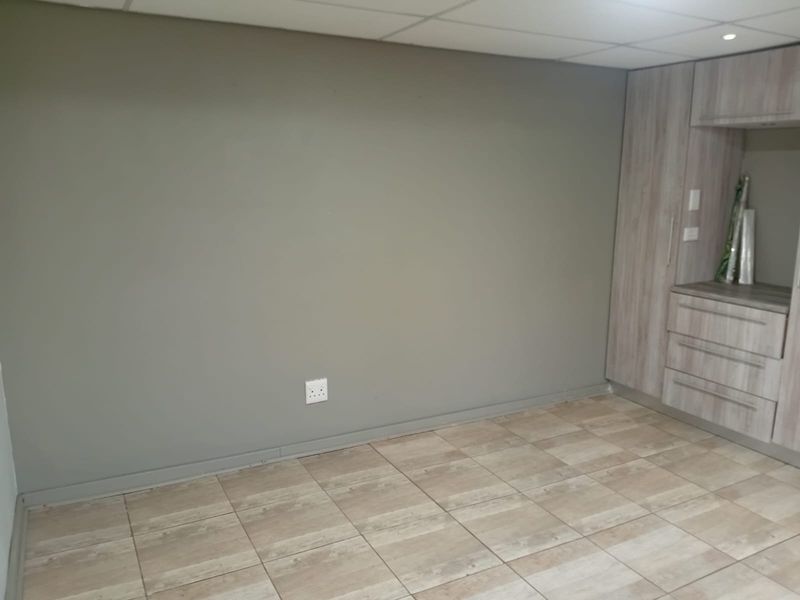 An empty bedroom featuring neutral tiled flooring, a drop ceiling, and built-in wooden cabinetry providing ample storage space.
