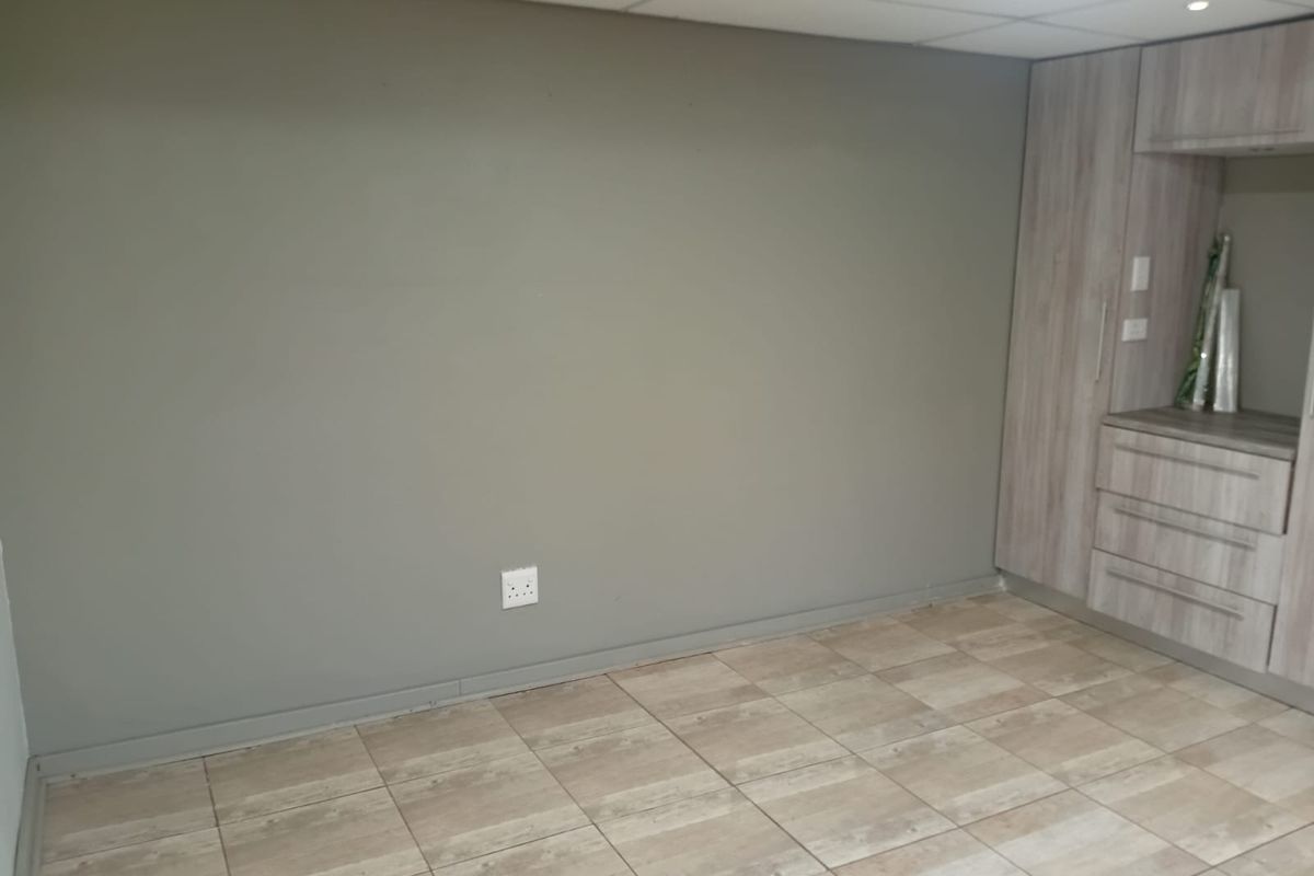 An empty bedroom featuring neutral tiled flooring, a drop ceiling, and built-in wooden cabinetry providing ample storage space.