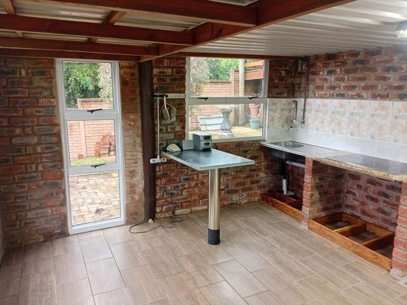 Rustic kitchen area featuring exposed brick walls, tiled flooring, timber ceiling beams, and a built-in sink unit with unfinished cabinetry base.