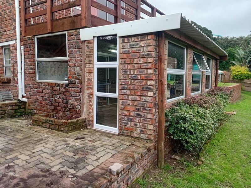 Rear exterior view of the property featuring exposed brickwork, a paved patio area, and a timber balcony structure with aluminium window frames.
