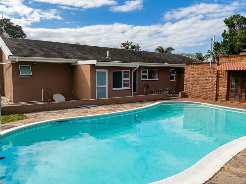 Rear exterior view featuring a swimming pool, paved patio area, and brick boundary wall with a covered entrance.