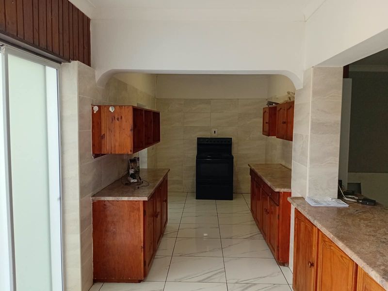 A functional kitchen featuring wooden cabinetry, stone-look countertops, a freestanding oven, and neutral tiled flooring throughout the space.