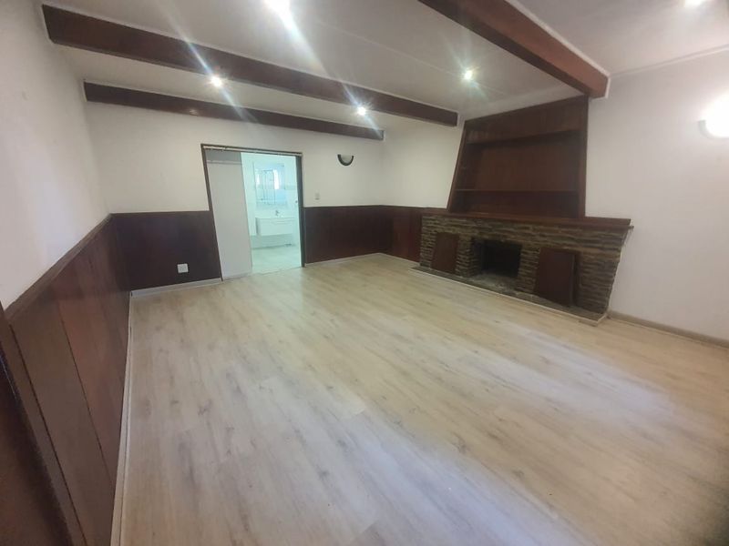 Spacious living room featuring exposed timber ceiling beams, a stone-clad fireplace with built-in shelving, and timber wall paneling.