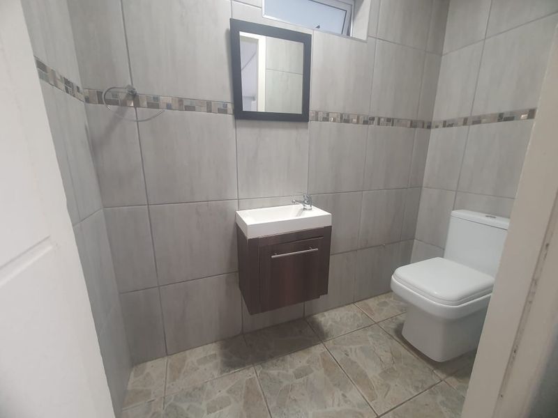 A clean, modern guest bathroom featuring neutral wall tiles, a wall-mounted vanity with basin, and a standard toilet.