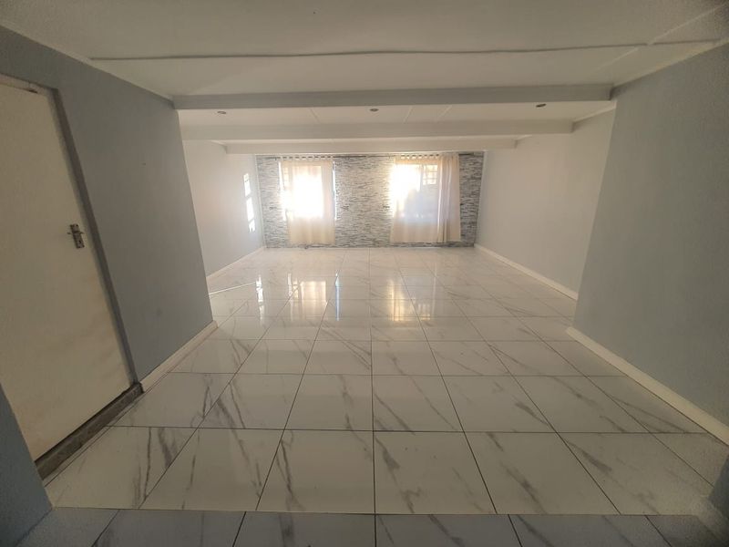 A spacious, empty living area featuring modern marble-look floor tiles, a stone-cladding feature wall, and recessed ceiling lighting.