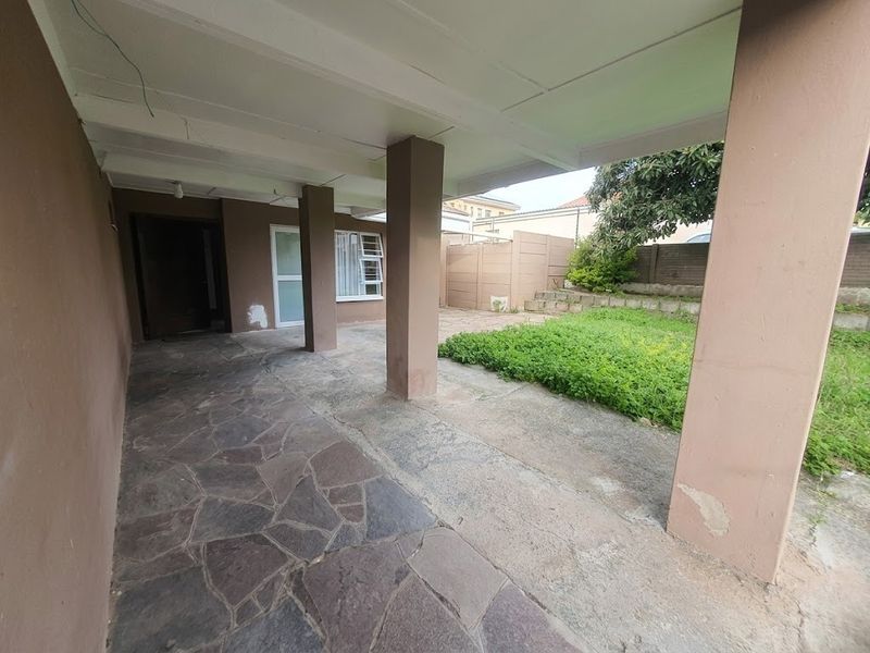 A covered outdoor patio area featuring stone paving and concrete pillars, leading out to a small garden space with a boundary wall.
