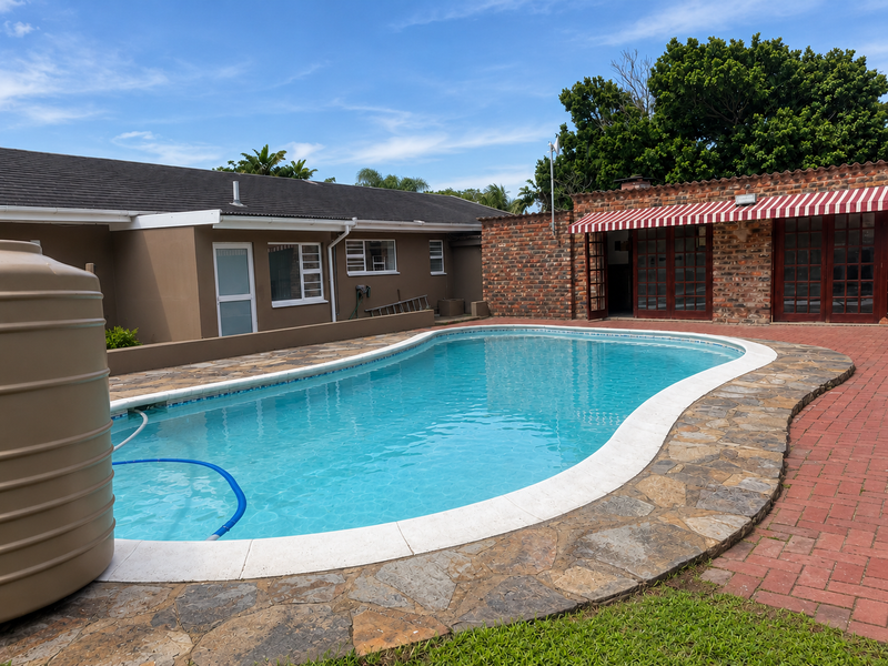 Outdoor pool area featuring a swimming pool with stone coping, brick paved surround, and an adjacent brick structure with an awning and french doors.
