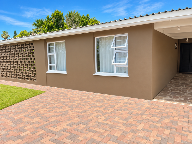 A well-maintained front exterior featuring a brick paved driveway, decorative breeze block wall, and modern aluminium window frames under a corrugated roof.