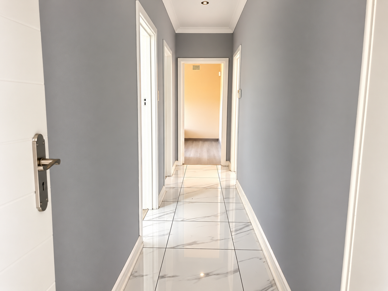 A bright, modern hallway featuring polished marble-look floor tiles, neutral grey walls, and clean white trim, leading to adjacent rooms.