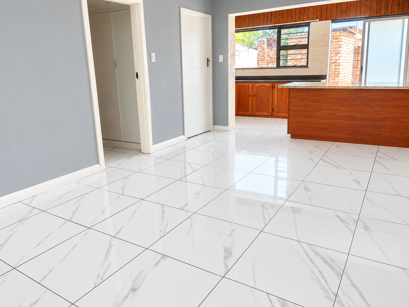 Spacious open-plan living area featuring modern marble-look floor tiles and a functional kitchen with wooden cabinetry and granite countertops.