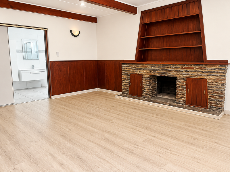 Spacious living room featuring a stone fireplace, built-in wooden shelving, and classic wood paneling, with direct access to an adjacent modern bathroom.