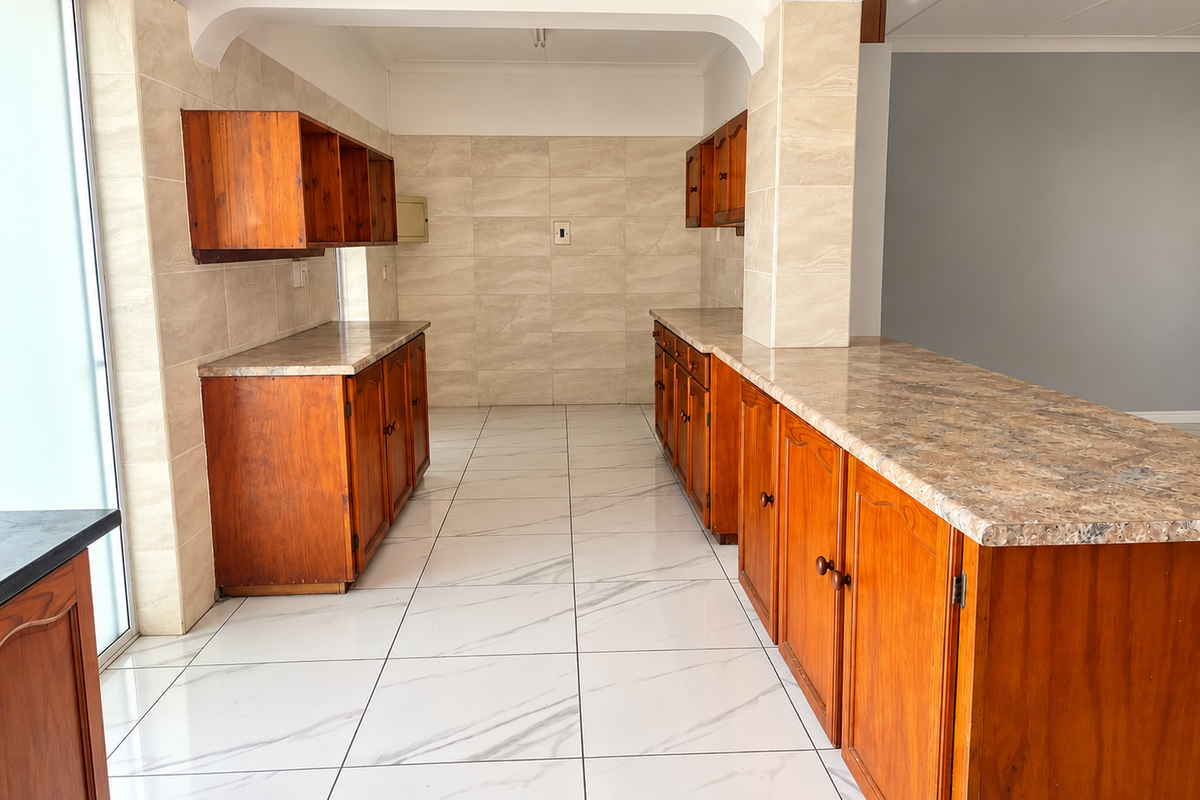 A spacious, empty kitchen featuring wooden cabinetry, laminate countertops, and modern white marble-look floor tiles, offering a clean canvas for potential updates.