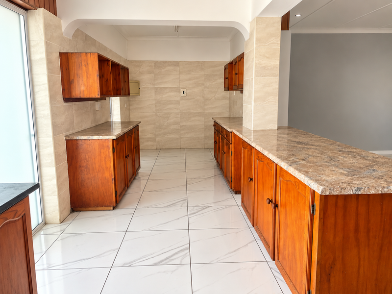 A spacious, empty kitchen featuring wooden cabinetry, laminate countertops, and modern white marble-look floor tiles, offering a clean canvas for potential updates.