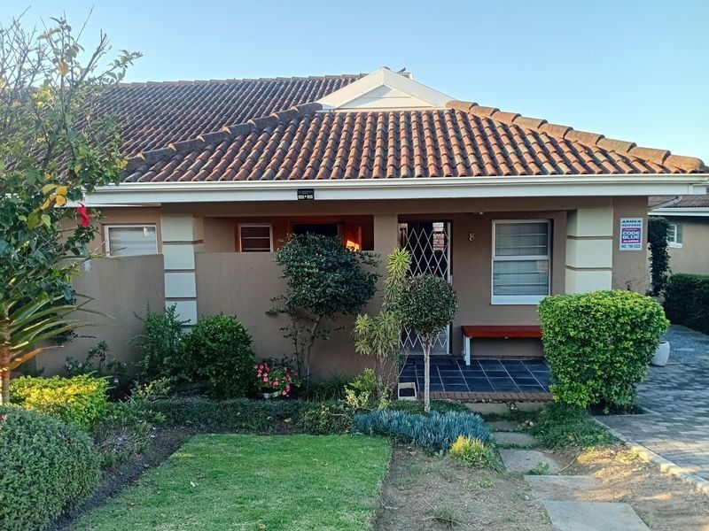 Front elevation of a townhouse featuring a tiled roof, paved entrance walkway, and security gate, set within a landscaped garden area.