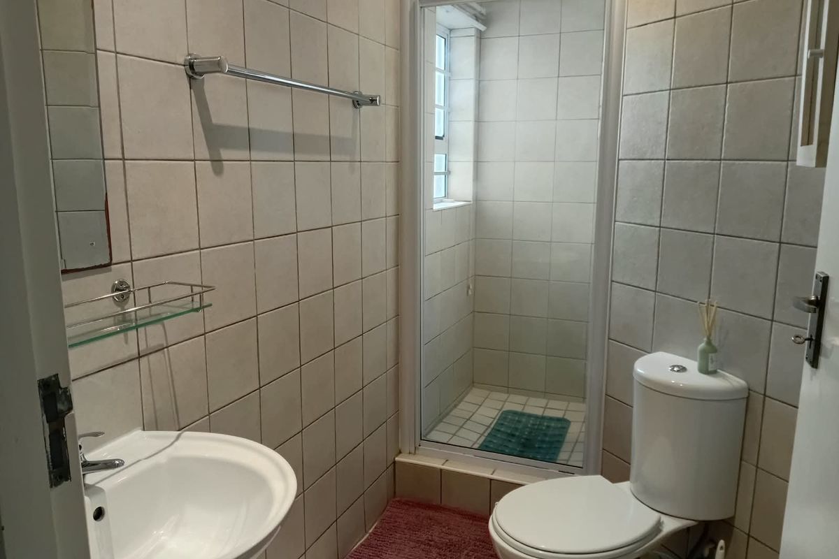 A functional bathroom featuring a pedestal sink, toilet, and a separate shower enclosure with tiled walls and flooring.