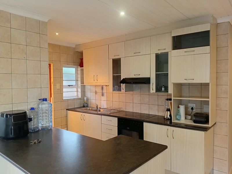 Functional kitchen featuring light-toned cabinetry, dark laminate countertops, integrated oven and hob, and tiled backsplash with ample storage space.
