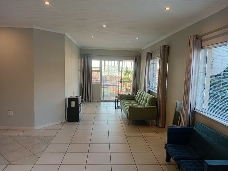 A bright living room featuring neutral tiled flooring, recessed downlighting, and a sliding glass door with security gate leading to an outdoor area.
